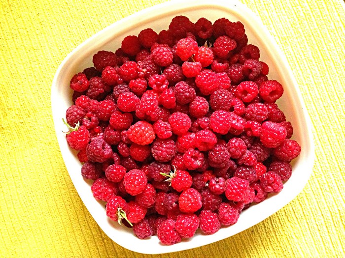 Bowl of fresh raspberries on a yellow surface