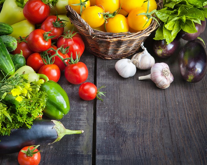 Vegetables including tomatoes, eggplants, bell peppers, and garlic on wood planks