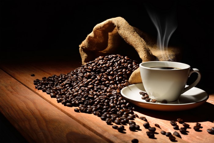 Coffee beans spilling from a burlap sack next to a steaming cup