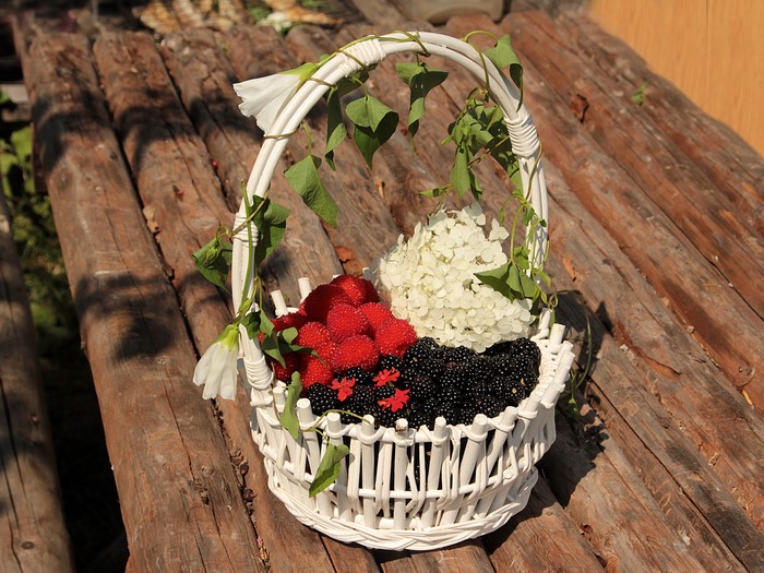Wicker basket with raspberries, blackberries, and hydrangea on wood planks