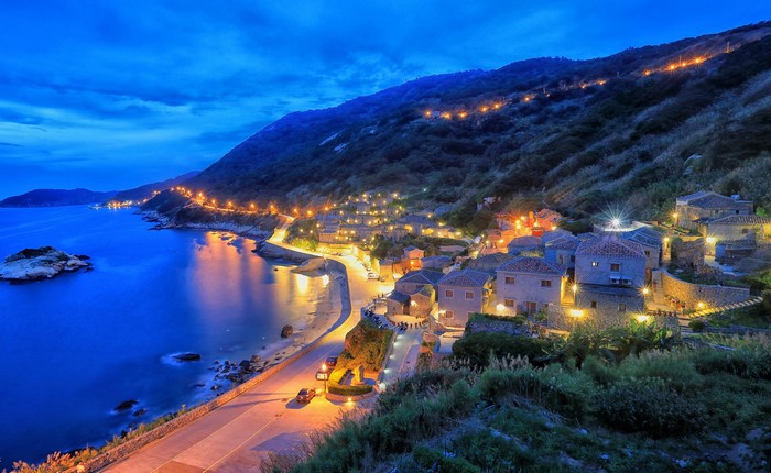Coastal village at dusk with illuminated houses on a hillside in Taiwan