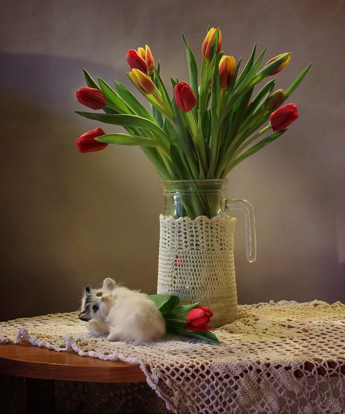 Tulips in a vase with a toy cat on a table