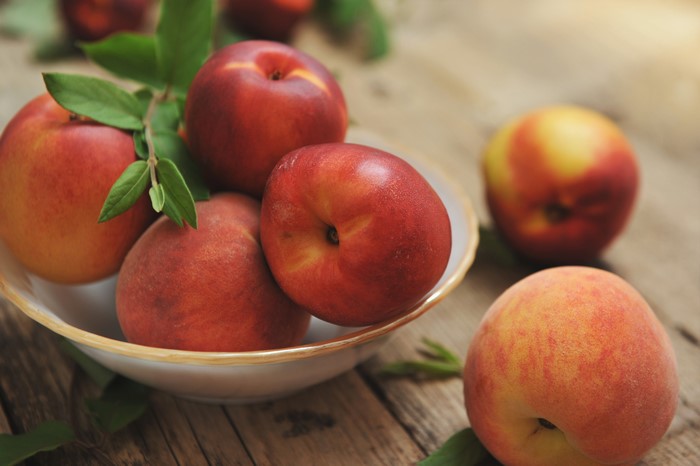 Peaches in a bowl on wood planks