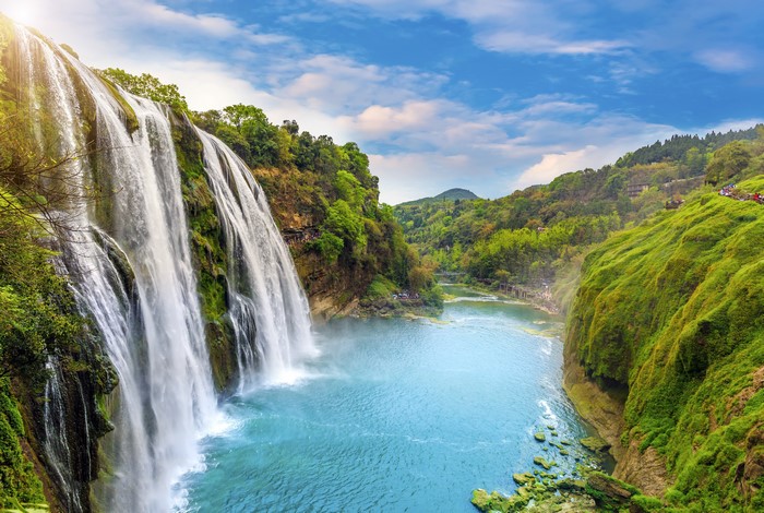 Waterfall scenery with lush green hills and blue sky