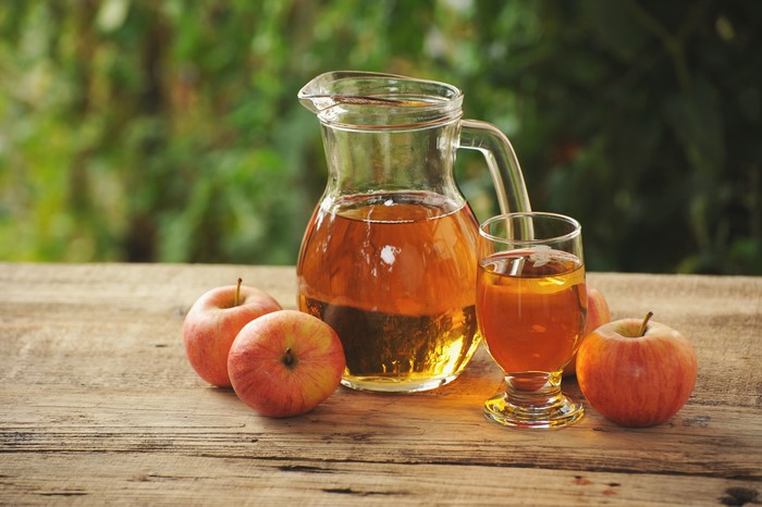 Apple juice in a jug and glass with apples on wood