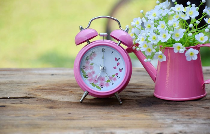 Pink alarm clock with flowers and watering can