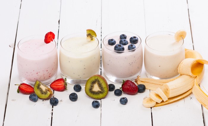 Four fruit smoothies with fresh fruit on a white wooden table