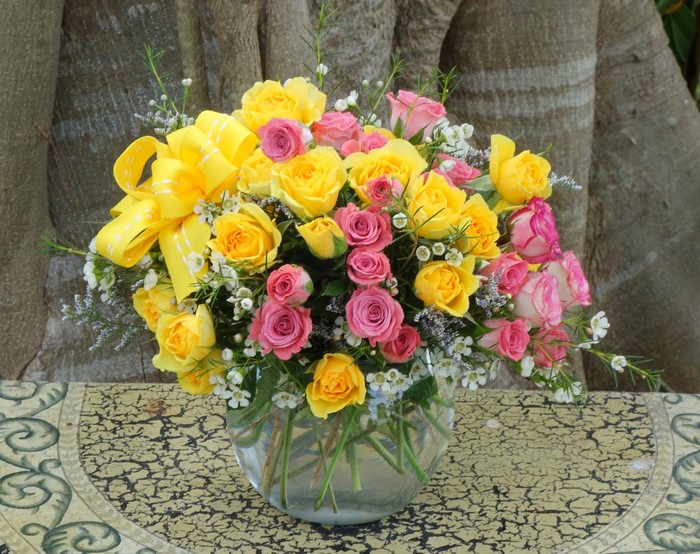 Yellow and pink roses in a glass vase with a yellow bow