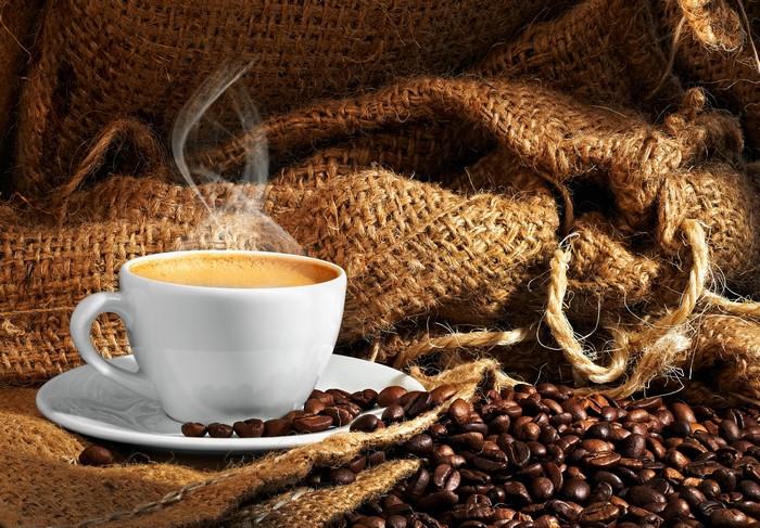 Coffee cup with steam and coffee beans on burlap