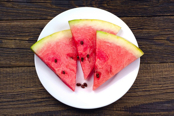 Watermelon slices on a white plate on wood planks