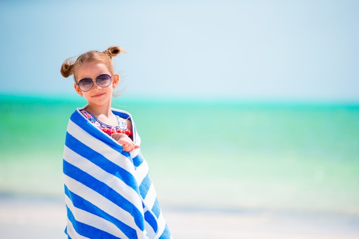 Little girl in towel and sunglasses on beach