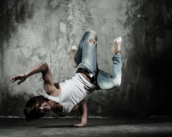 Man breakdancing in a singlet and ripped jeans