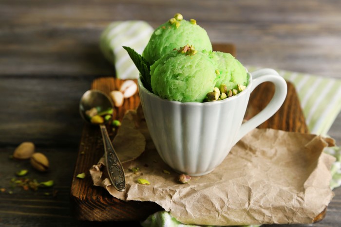 Pistachio ice cream in a cup with nuts and spoon