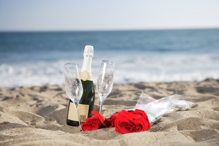 Champagne bottle, glasses, and roses on a beach