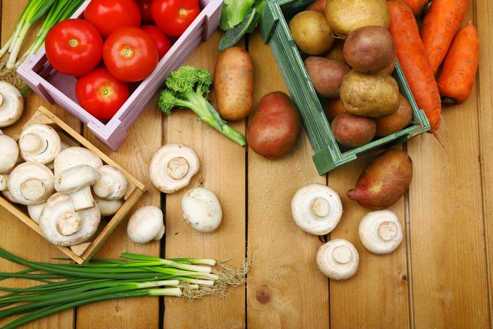 Vegetables including potatoes, mushrooms, tomatoes, carrots, and green onions on wood planks