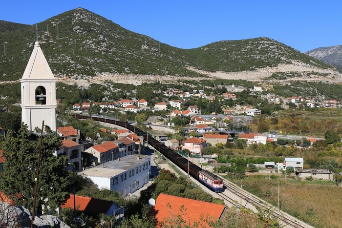Train passing through a village with a church tower and mountains
