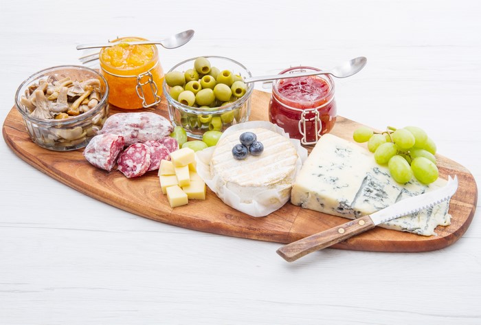 Cheese board with olives, sausage, jam, mushrooms, and grapes