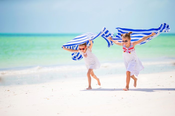 Two girls running on a beach with a towel
