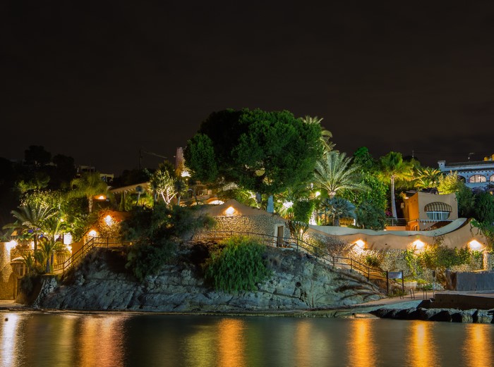 Illuminated houses and trees on a rocky coast at night in Calp, Spain