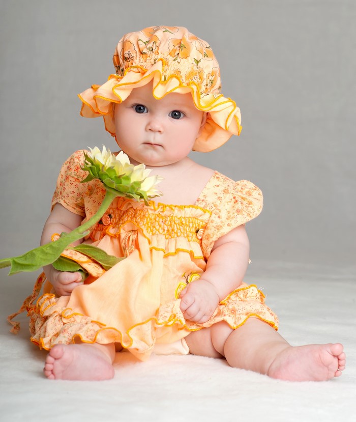 Baby in a sunflower dress and hat holding a sunflower