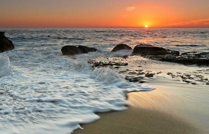 Sunset over the ocean with waves crashing on rocks and sand