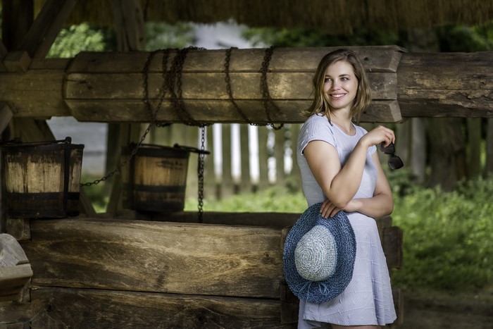 Woman with hat and sunglasses by a water well
