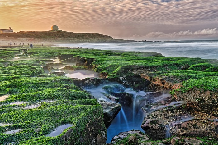 Green mossy rocks and ocean with radar dome on hill, Taiwan