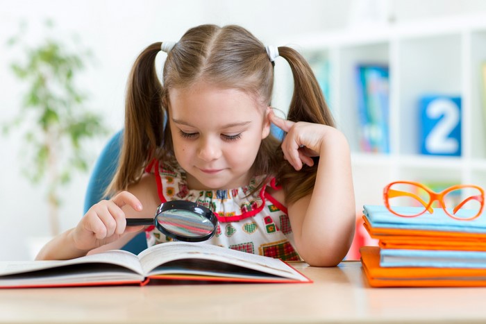 Girl with magnifying glass reading a book