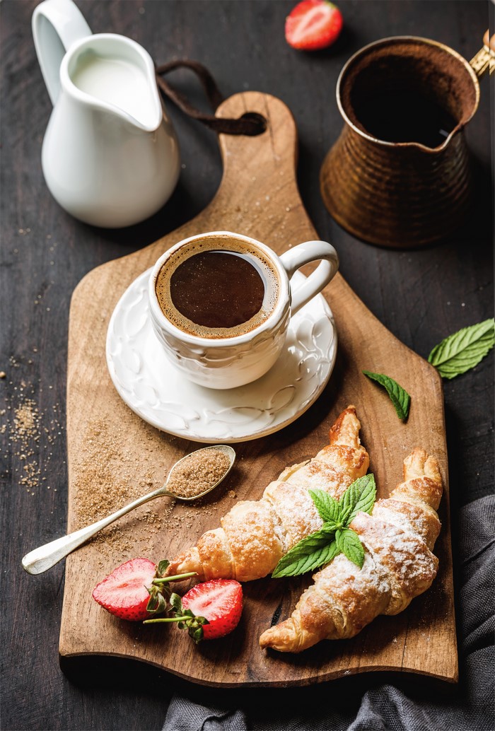 Coffee and croissants with strawberries on a cutting board