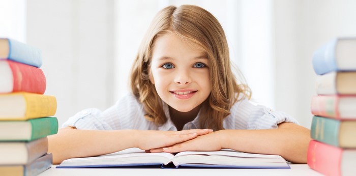 Smiling Girl Reading Book Surrounded by Stacked Books