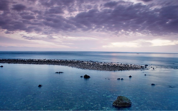 Calm sea with rocks and purple clouds at sunset
