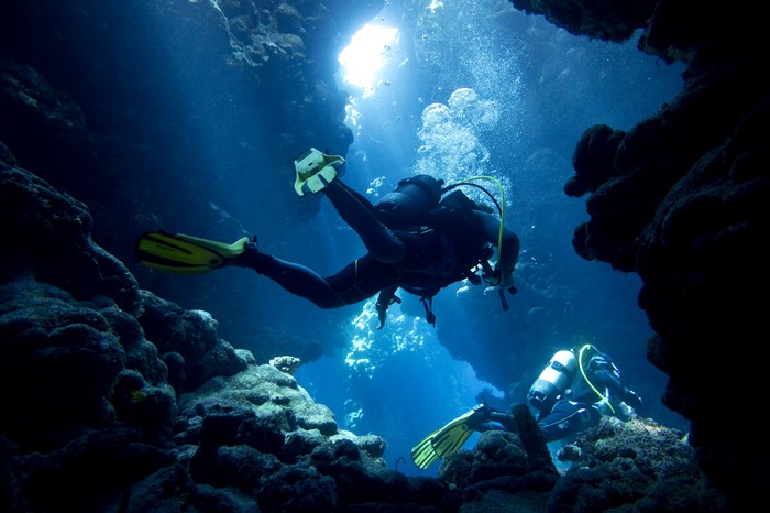 Divers exploring a dark underwater cave with light shining through