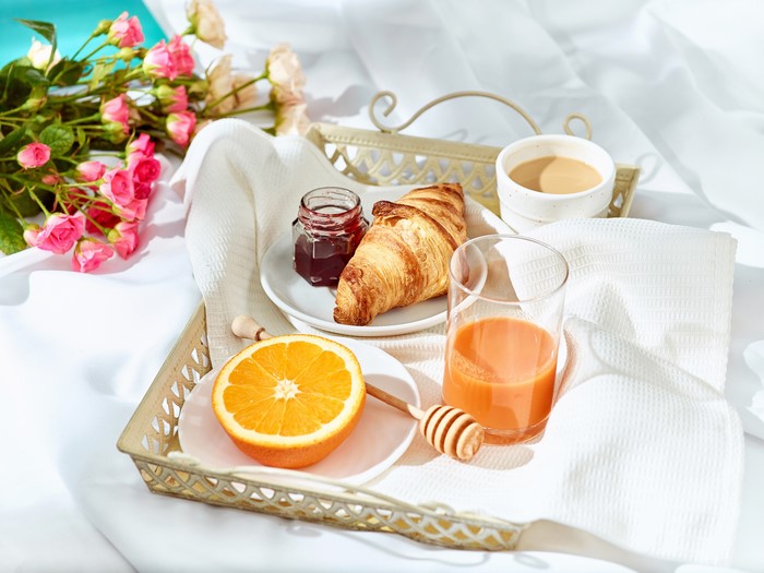 Breakfast tray with croissant, juice, coffee, and flowers