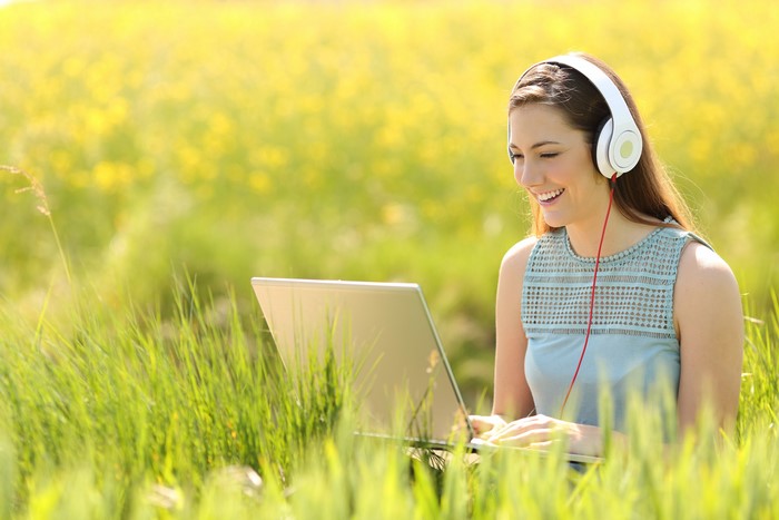 Woman with headphones using a laptop in a field