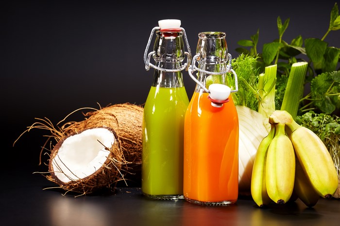 Two bottles of juice with bananas, coconuts, and vegetables
