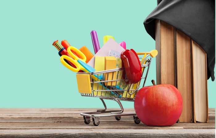 School supplies in a shopping cart with books and apple