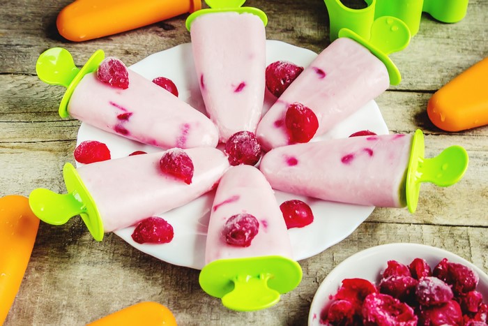 Pink berry popsicles on a white plate with raspberries