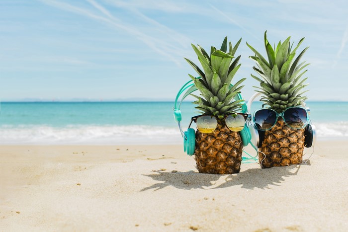 Two pineapples with sunglasses and headphones on a beach
