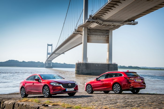 Two red Mazda 6 cars parked near a bridge