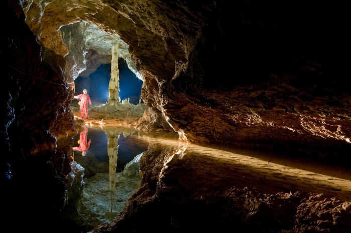 Person in a cave with a pool of water and stalagmites
