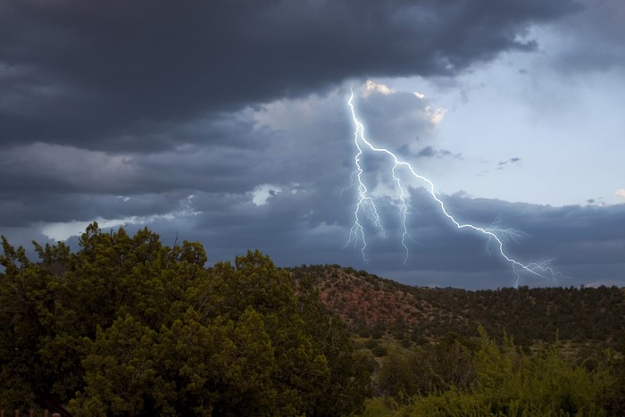 Lightning strikes over a forested landscape under stormy clouds