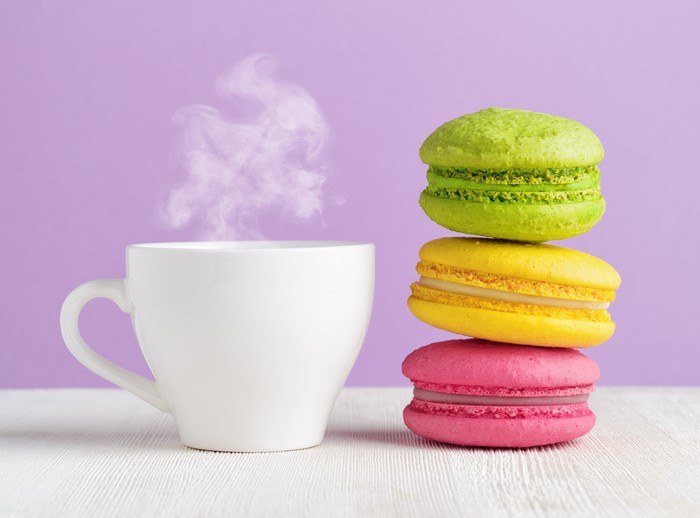 White cup with steam and colorful macarons