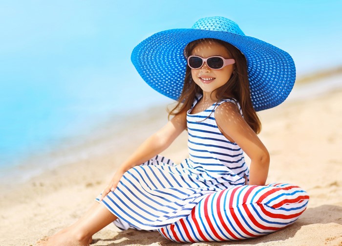 Girl in a blue hat and striped dress on the beach