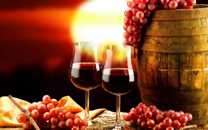 Two glasses of red wine with a barrel and grapes