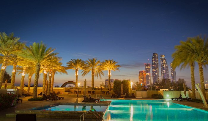 Resort pool at night with palm trees and city skyline