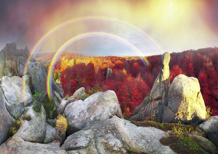 Autumn forest with double rainbow over rocky mountains in Ukraine