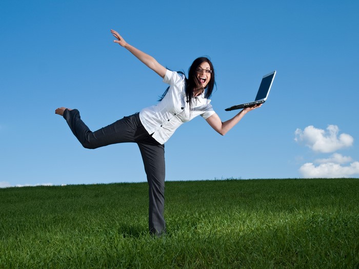 Brunette woman with glasses holding a laptop in a field