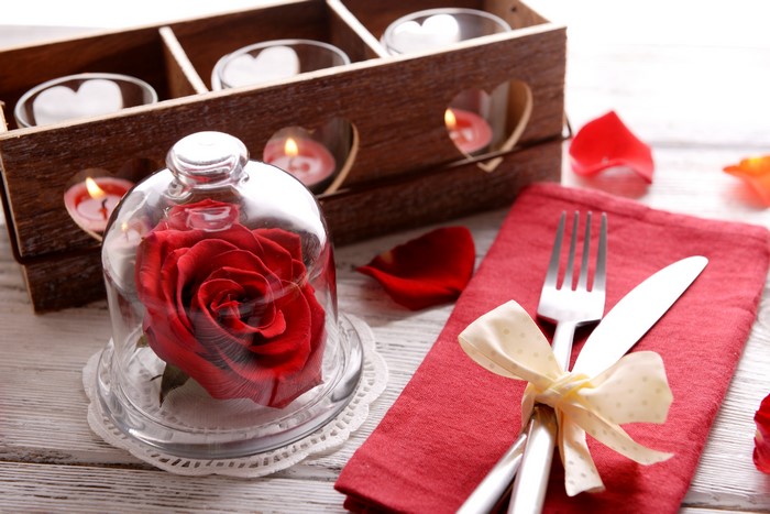 Red rose under glass dome with candles and cutlery