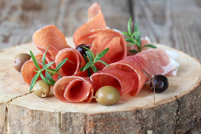 Sliced ham with olives and rosemary on wood