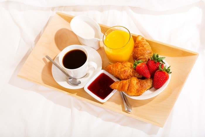 Breakfast tray with coffee, juice, croissants, jam, and strawberries